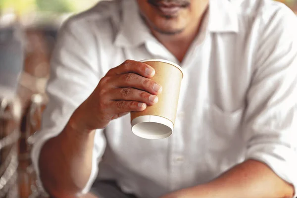 Zbliżenie młodego mężczyzny trzymającego kawę do zabrania wczesnym rankiem w domu, zamazane tło. — Zdjęcie stockowe