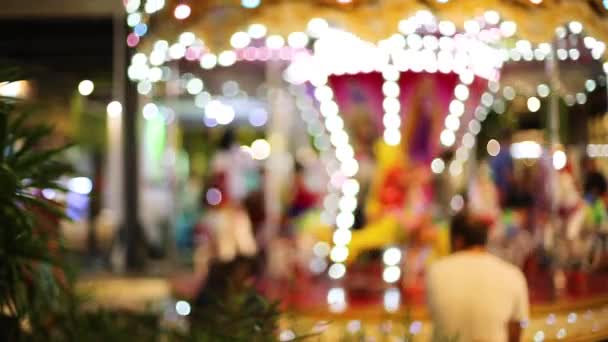 Blur kind spelen op carrousel en bokeh van licht 's nachts. — Stockvideo