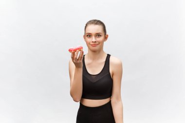 Güzel fitness modeli siyah bir fitness kıyafeti giyiyor ve elinde abur cubur var. Gri arkaplan üzerinde izole.