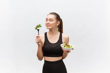 Beyaz arka planda salata yiyen genç ve güzel bir spor kadını..