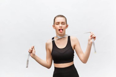 Üç mezurayla boyunu ölçen güzel, formda bir kız üzgün bir ifadeyle aşağıya bakıyor. Beyazda izole edilmiş