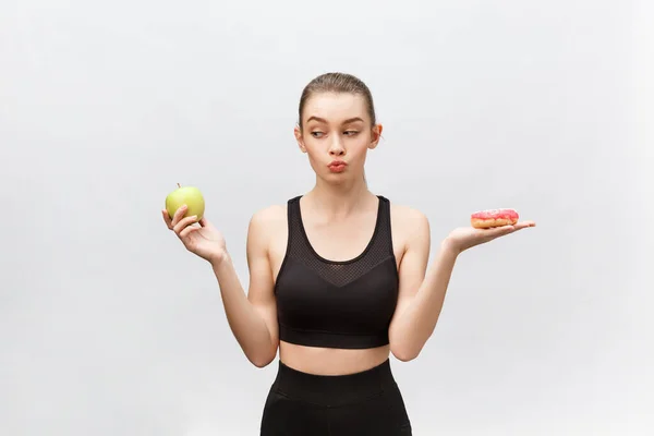 Mujer joven eligiendo entre donut y manzana sobre fondo blanco. Concepto de alimentación dietética —  Fotos de Stock