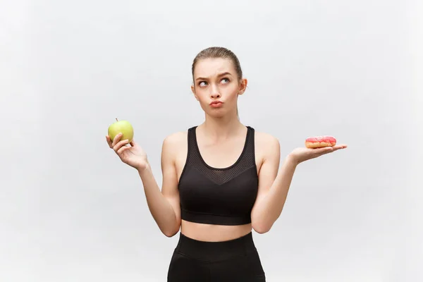 Mujer joven eligiendo entre donut y manzana sobre fondo blanco. Concepto de alimentación dietética —  Fotos de Stock