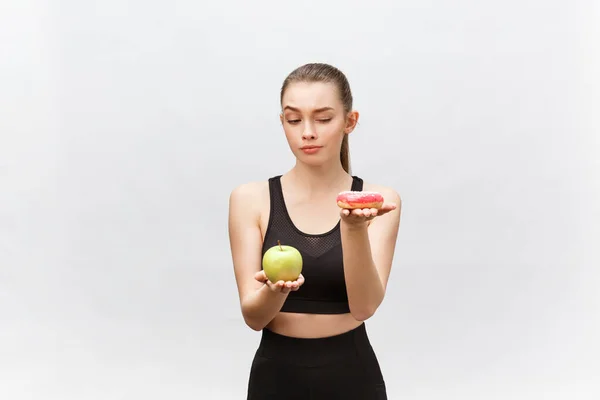 Jovem mulher escolhendo entre donut e maçã no fundo branco. Conceito alimentar dietético — Fotografia de Stock