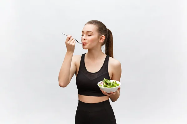 Joven hermosa mujer del deporte comiendo ensalada sobre fondo blanco . —  Fotos de Stock