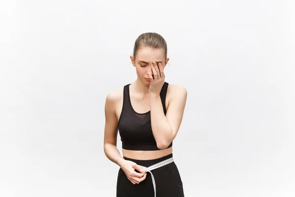 Young woman with excess weight in sporty top sadly looking on result of measuring waist over white background — Stock Photo, Image