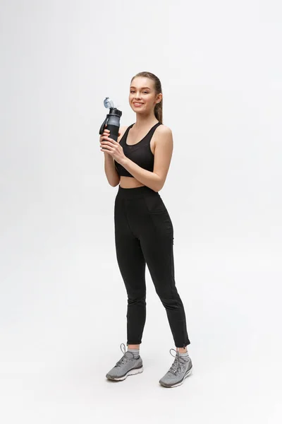 Retrato de una joven deportista sana sosteniendo una botella de agua aislada sobre un fondo blanco — Foto de Stock