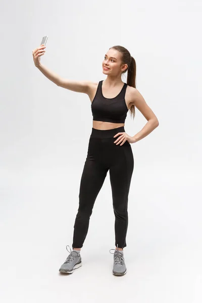 Mujer deportiva haciendo foto selfie en el teléfono inteligente aislado sobre un fondo blanco . — Foto de Stock