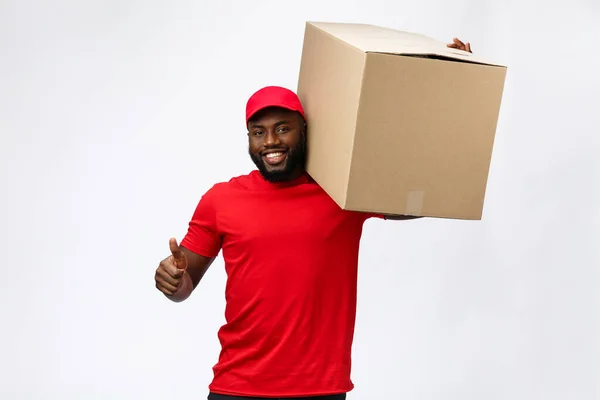 Conceito de entrega - Bonito homem de entrega afro-americano transportando caixa de pacote. Isolado no estúdio Grey Background. Espaço de cópia — Fotografia de Stock