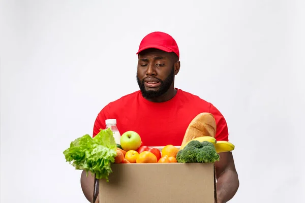 Портрет доставки африканского американца в красной рубашке. он поднимает тяжелые продуктовые коробки против того, чтобы изолировать на белом фоне. — стоковое фото