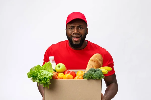 Молодой африканский американец держит коробку с продуктами в руках с шокирующим лицом. Изолированный на сером фоне. — стоковое фото