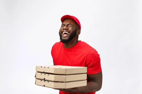 Φωτογραφία του χαρούμενου Αφροαμερικανού από την υπηρεσία παράδοσης σε κόκκινο t-shirt και καπάκι δίνοντας παραγγελία τροφίμων και κρατώντας κουτιά πίτσα απομονώνονται σε λευκό φόντο — Φωτογραφία Αρχείου