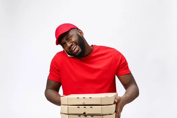 Delivery Concept: Όμορφος Αφρικανός ντελιβεράς πίτσας που μιλάει στο κινητό με σοκαριστική έκφραση προσώπου. Απομονωμένα σε γκρι φόντο. — Φωτογραφία Αρχείου