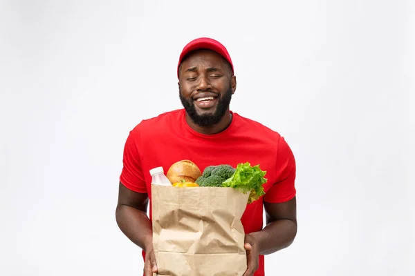 Молодой африканский американец держит пакет с продуктами в руках с шокирующим лицом. Изолированный на сером фоне. — стоковое фото