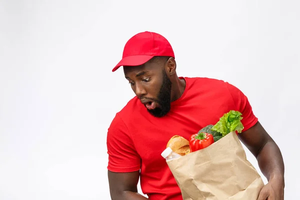 Jovem afro-americano segurando pacote de supermercado em mãos com rosto chocante. Isolado sobre fundo cinza . — Fotografia de Stock