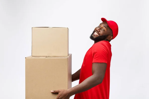 Retrato da entrega homem americano africano em camisa vermelha. ele levantando caixas de peso pesado contra ter um isolado no fundo branco . — Fotografia de Stock