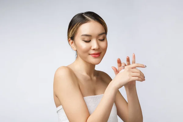 Азиатка наносит косметический крем на кожу на изолированном белом фоне — стоковое фото