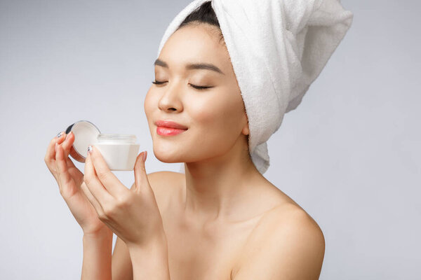 концепция здоровья и красоты - привлекательная азиатская женщина наносит крем на кожу, изолированный на белом.