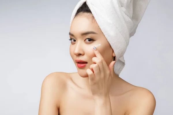 Концепція здоров'я та краси - приваблива азіатська жінка наносить крем на її шкіру, ізольована на білому . — стокове фото