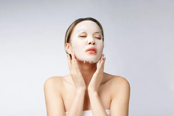 सुंदर एशियाई महिला अपने चेहरे पर कागज शीट मास्क लागू कर रही है सफेद पृष्ठभूमि — स्टॉक फ़ोटो, इमेज