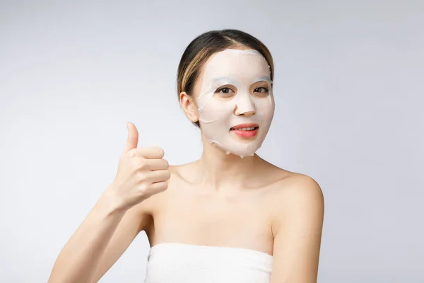 Lázně, zdravotní péče. Asijské dívka s kosmetickou maskou s ukazující palec nahoru. — Stock fotografie