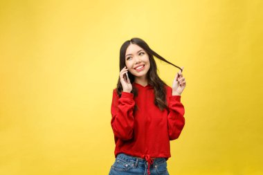 Sarı arka planda izole edilmiş cep telefonuyla konuşan neşeli genç bir kadın.