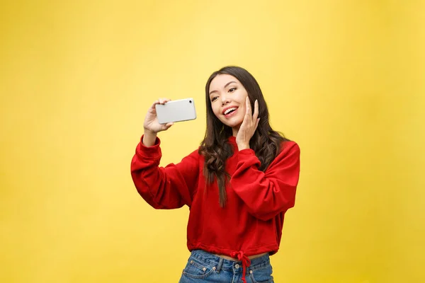 Smiling young girl making selfie photo on smartphone over yellow background — Stock Photo, Image