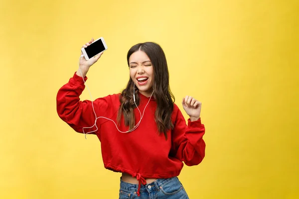 Retrato de una mujer feliz escuchando música en auriculares y bailando aislada sobre un fondo amarillo — Foto de Stock