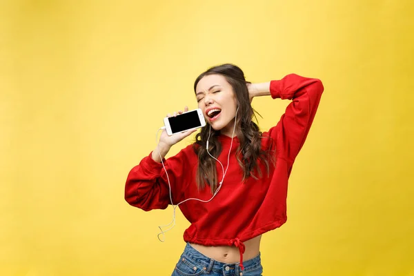 Retrato de una mujer feliz escuchando música en auriculares y bailando aislada sobre un fondo amarillo — Foto de Stock