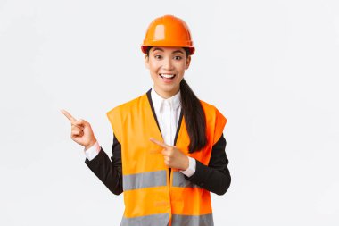 İnşaat, inşaat ve endüstriyel konsept. Kasklı gülümseyen kadın mühendis ve yansıtıcı giysiler yolu gösteriyor, sol üst köşeyi işaret ediyor, projeden bahsediyor, beyaz arka plan.