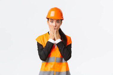 Endişeli ve endişeli Asyalı kadın mühendis inşaat alanında sorun yaşıyor, nefes darlığı çekiyor ve ağzını kapatıyor şok geçiriyor, kameraya paniklemiş bir ifadeyle bakıyor, güvenlik kaskı takıyor.