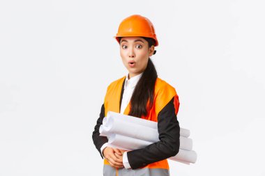Güvenlik kaskı ve yansıtıcı ceketli Asyalı kadın mimar şaşırmış ve heyecanlı. İnşaat alanını planlarıyla ziyaret ediyor, eğleniyor gibi görünüyor.