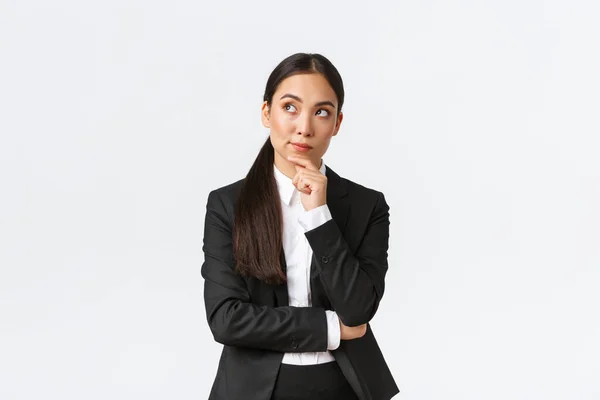 Smart professional female architect, industrial woman in suit thinking about solution, looking upper left corner and touching chin thoughtful, making-up plan, standing white background