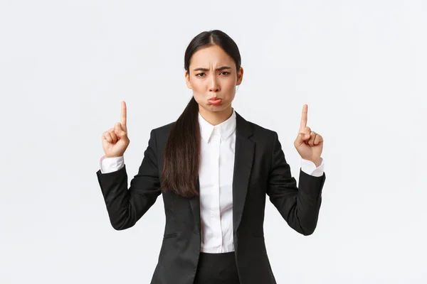 Csalódott duzzogó ázsiai női vállalkozó öltöny panaszkodik és duzzog a kudarc, ujjal felfelé, grimaszoló elégedetlen, érzés le a megbánás, álló fehér háttér — Stock Fotó