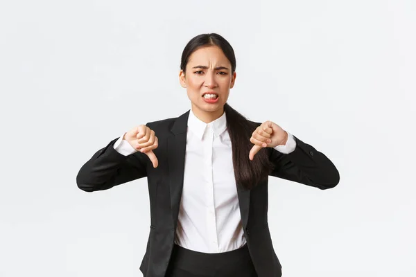Disappointed skeptical and upset asian saleswoman complaining on bad product or service, showing thumbs-down and grimacing displeased, complitely dissatisfied standing over white background — Stock Photo, Image