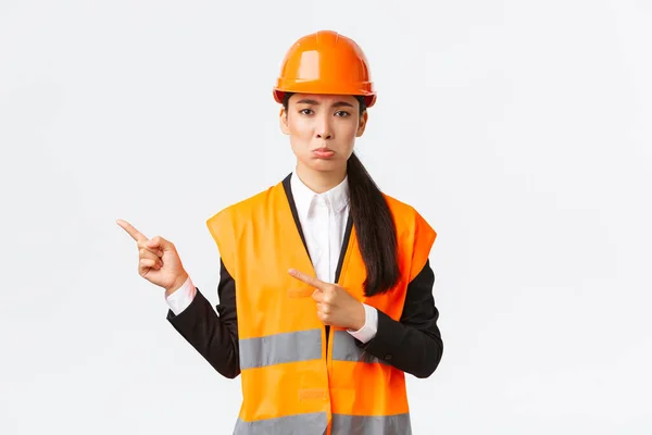 Будівництво, будівництво та промислова концепція. Ненажерлива жінка-інженер у відбиваючому одязі та шоломі, вказуючи пальці у верхньому лівому куті, розчаровуючись, показуючи щось погане — стокове фото
