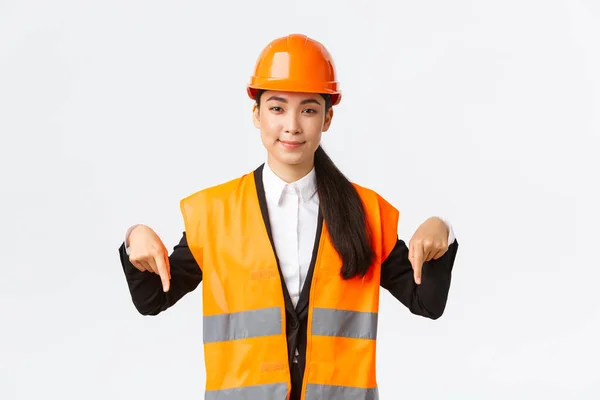 建築、建設、産業の概念。成功した女性エンジニア、彼女の不動産プロジェクトを示す建築家、指を下に向け、家を売り、安全ヘルメットと反射服を身に着けている — ストック写真