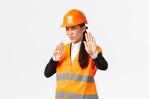 Descontente e relutante asiático arquiteto feminino em segurança capacete grimacing de aversão, mostrando parar gesto, recusar ou rejeitar terrível plano nojento, de pé desapontado fundo branco — Fotografia de Stock