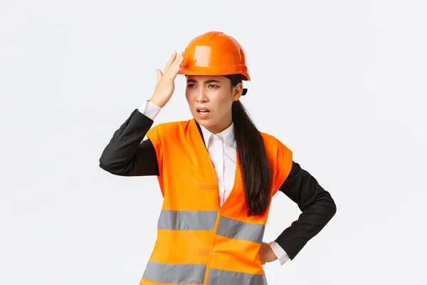 Озвучена і розчарована жінка азіатський головний інженер, що виганяє будівельників, робить дурну помилку, шолом і виглядає засмученою, божевільною на архітекторі, стоячи на білому тлі — стокове фото