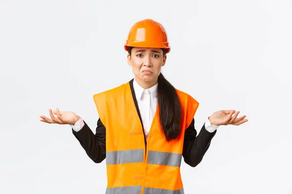 Upset and confused asian female engineer feeling complicated, raising hands sideways and shrugging, dont know why, have no idea, being clueless, pouting and being sad, white background