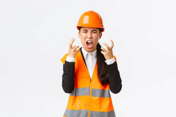 Mad and outraged asian female chief engineer, construction manager burst in rage, losing temper at employees, shouting and shaking hands aggressive, scream furious as scolding someone