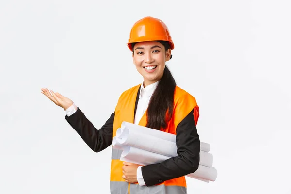 Souriant professionnel asiatique architecte femme, ingénieur en casque de sécurité présenter projet de construction, pointant la main gauche comme porter le plan directeur, donnant la parole, présenter la carte ou le plan du bâtiment — Photo