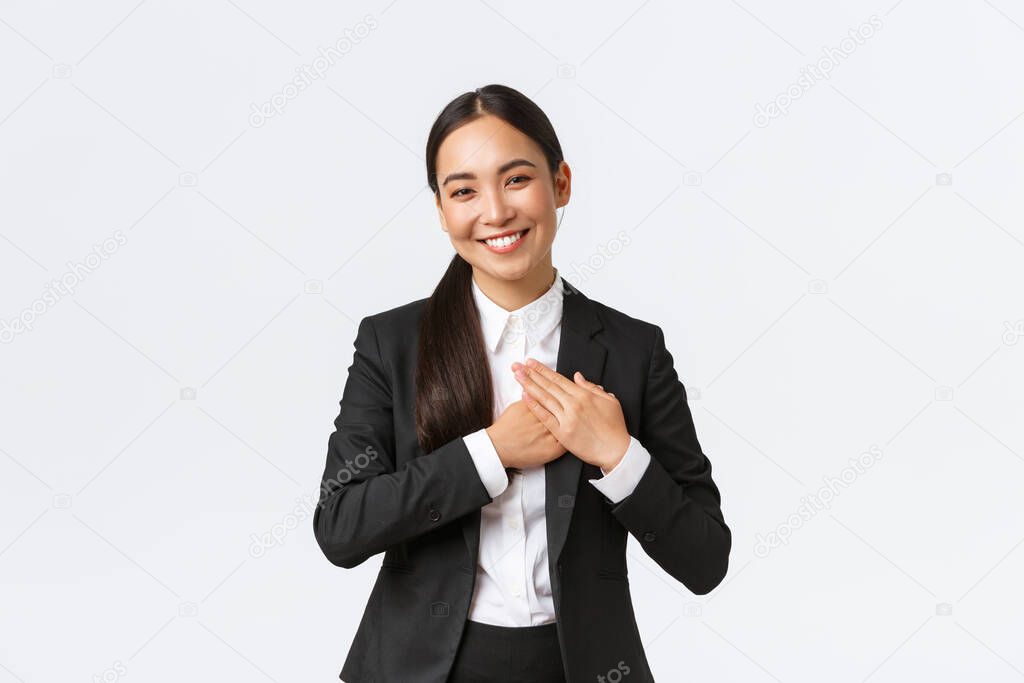 Happy pleased asian female entrepreneur love her clients, feeling flattered as receive praises with great job, holding hands on heart and smiling thankful, being grateful and appreciate efforts