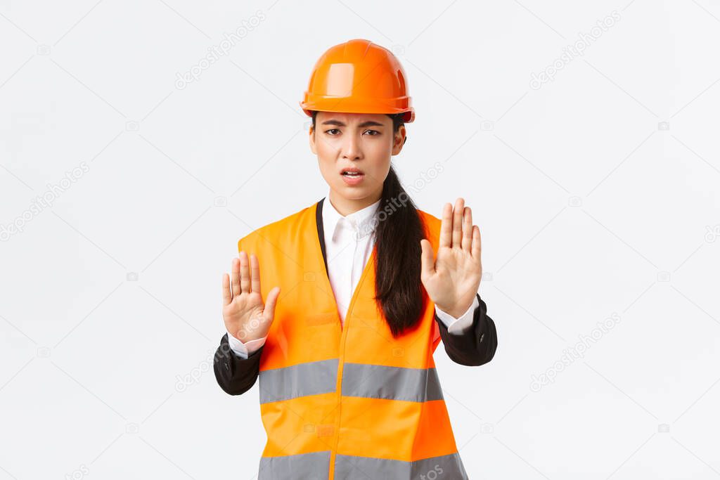 Disappointed angry asian female engineer in safety helmet and reflective clothing saying stop, prohibit and disagree with construction manager, showing enough, no gesture, white background