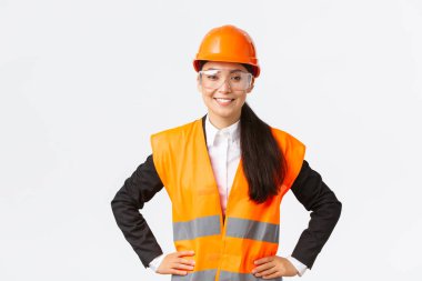 Kendine güvenen Asyalı kadın mimar, güvenlik kasklı inşaat mühendisi, koruyucu gözlükler teftiş için inşaat alanına girmeye hazır, çalışmanın sonuçlarından memnun, beyaz arka plan