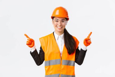Gülümseyen Asyalı kadın müteahhit, güvenlik kasklı mühendis, koruma gözlüğü yana bakan, sol ve sağ projeyi gösteren, inşaat projelerini tanıtan, beyaz arka plan