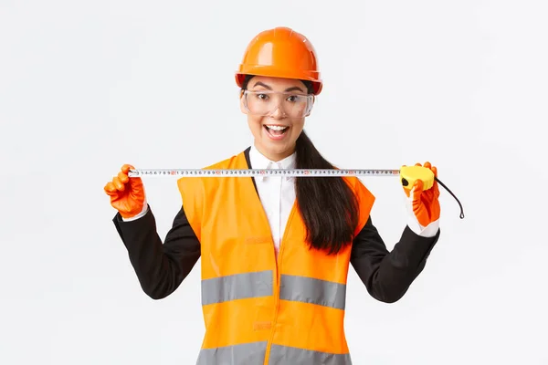 Excité et optimiste asiatique femme ingénieur de construction mesure disposition, tenant mètre ruban et sourire, prêt pour le travail à construire quelque chose, debout sur fond blanc dans le casque de sécurité — Photo