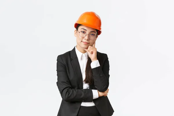 笑顔のプロのアジアの実業家は、建設にお金を投資し、企業での仕事を管理し、安全ヘルメットとスーツを着て、カメラを見て満足して、白い背景に立って — ストック写真
