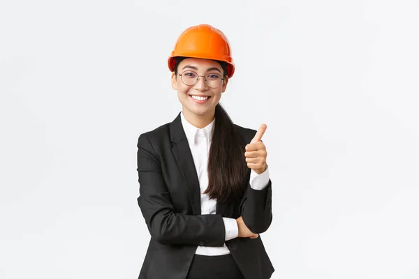 Zufriedene asiatische Unternehmerin inspiziert Unternehmen, freut sich über Bauarbeiten, zeigt Daumen hoch in Zustimmung, lächelt erfreut, sagt gut gemacht, gute Arbeit, garantiert Fertigstellung rechtzeitig — Stockfoto