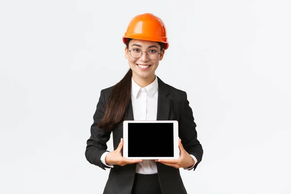 Lächelnde professionelle asiatische Architektin stellt ihr Projekt vor, Ingenieurin zeigt Diagramm auf digitalem Tablet-Bildschirm, macht Präsentation in Unternehmen oder Fabrik, steht weißer Hintergrund — Stockfoto